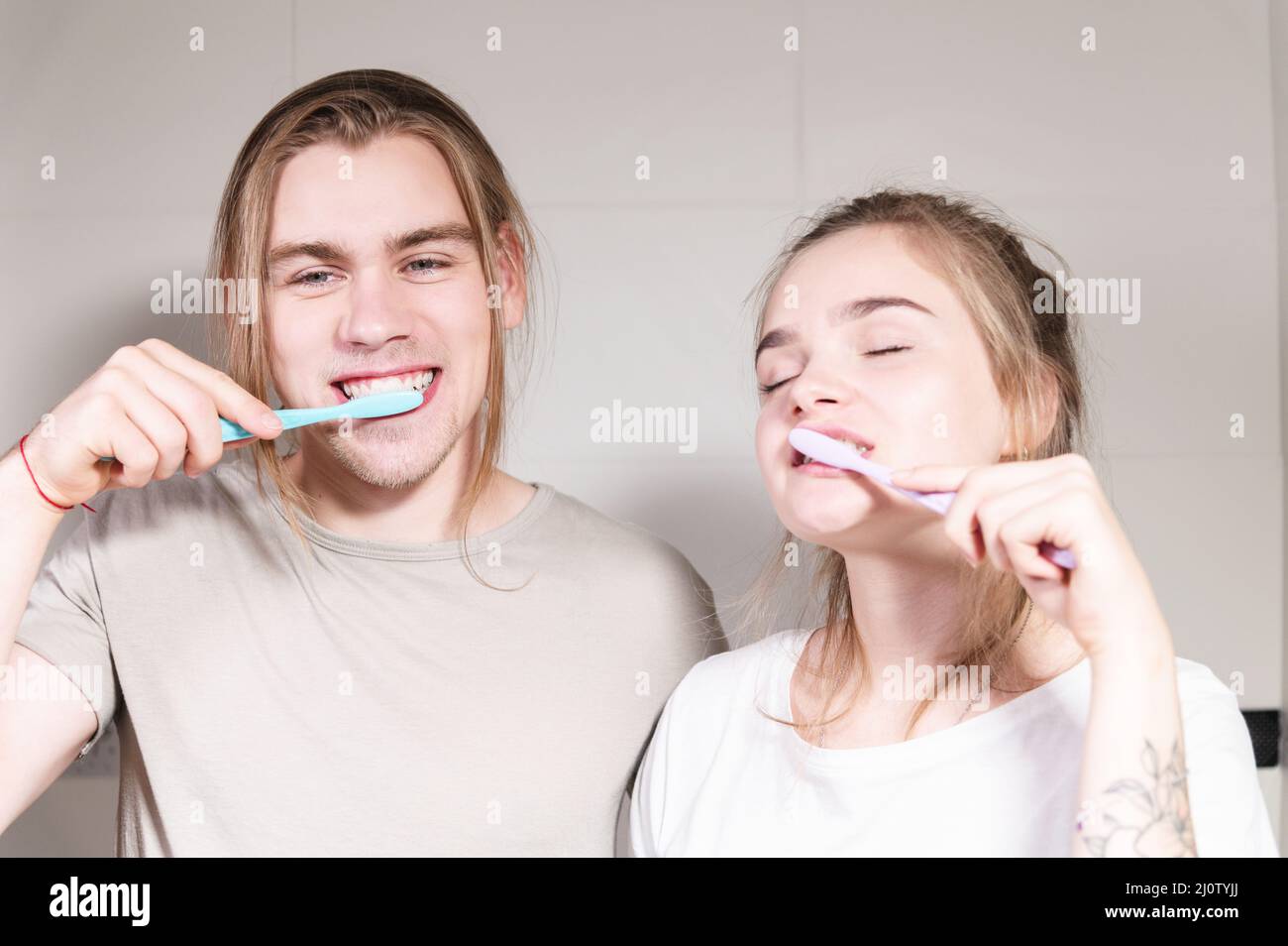 Un par joven de mellils de pelo largo se cepilla los dientes en el baño por la mañana. Una sonrisa sana y cuidado dental y oral Foto de stock