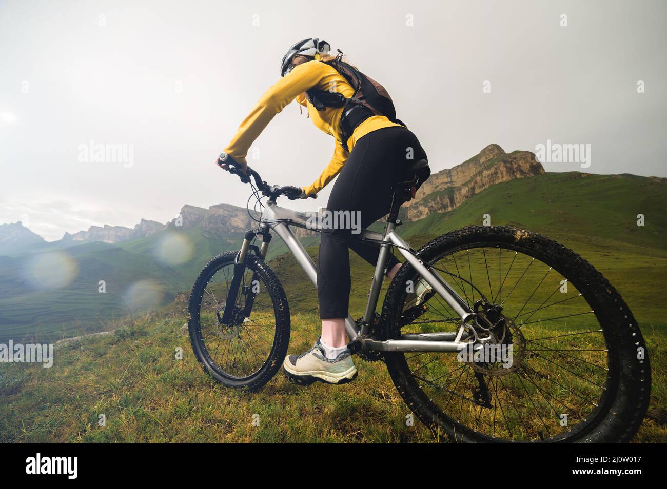 Atractiva chica de pelo rojo en un casco y con una mochila se sienta en una  bicicleta de montaña en las montañas con el telón de fondo de la roca  Fotografía de