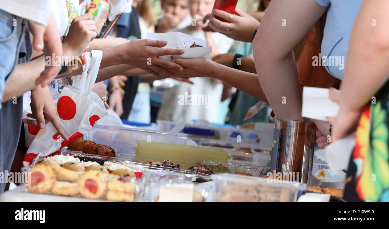 Un primer plano de las manos y el intercambio de alimentos en una feria comunitaria, fete o puesto de mercado. Una venta típica de pasteles o horneados. Foto de stock
