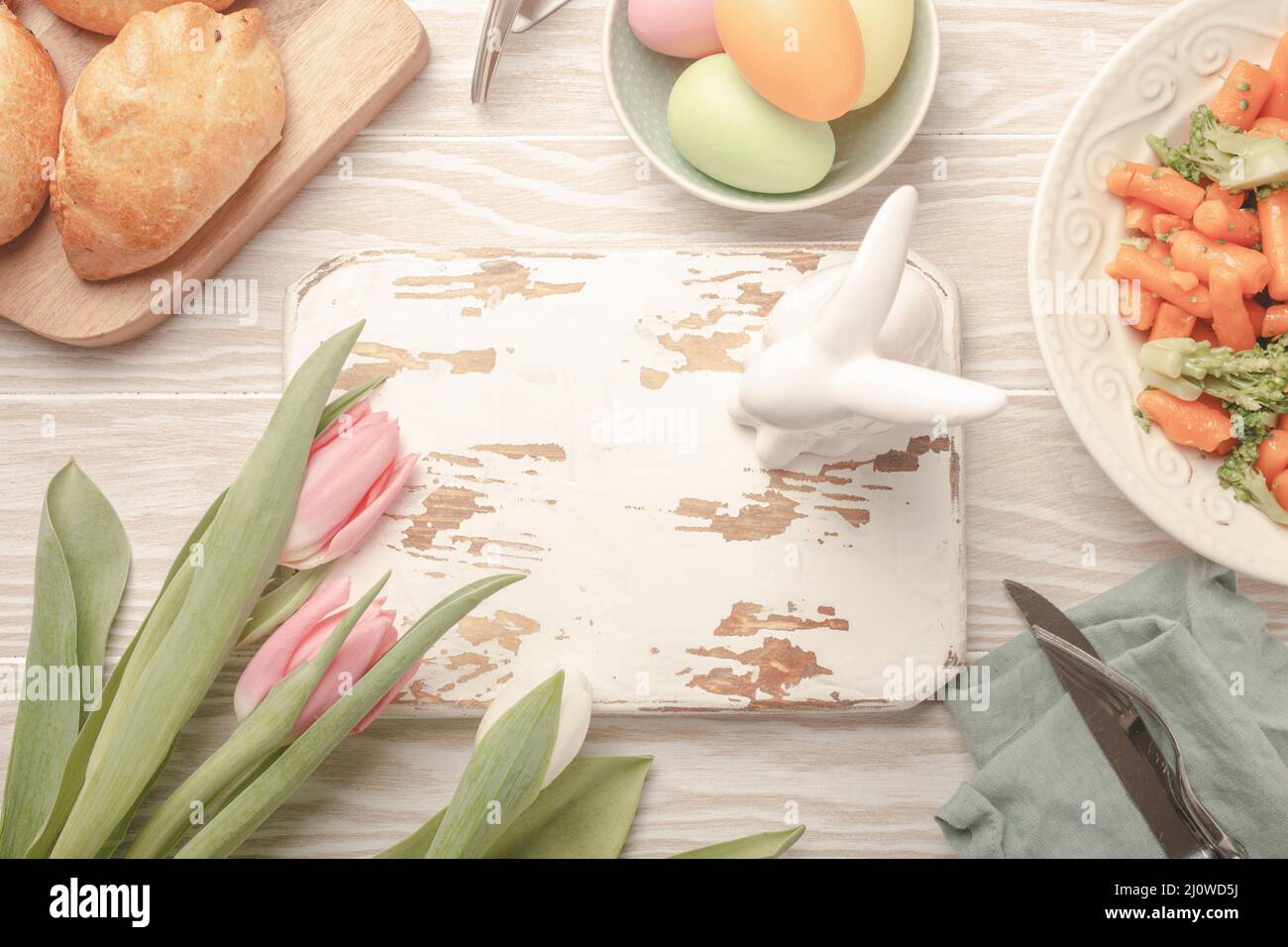 Tabla de cortar de madera blanca vacía y comida de Pascua en mesa de cocina Foto de stock