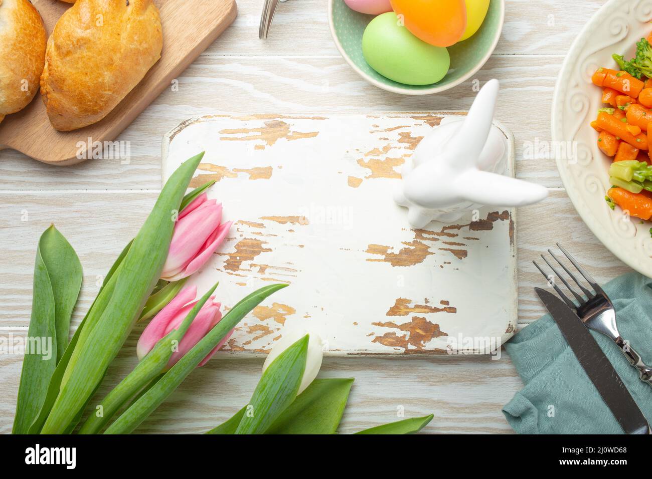 Tabla de cortar de madera blanca vacía y comida de Pascua en mesa de cocina Foto de stock