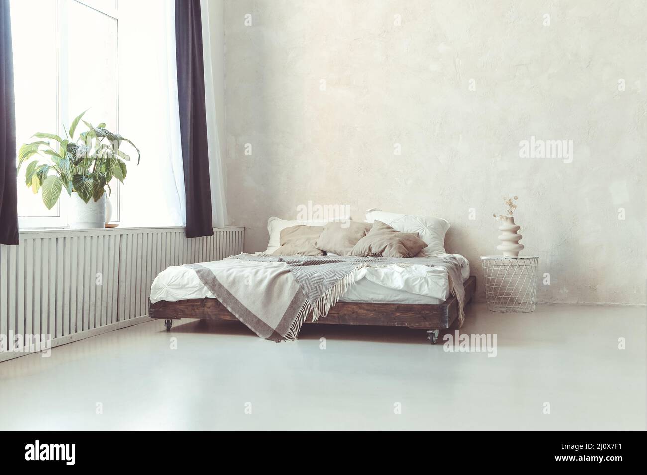 Dormitorio de estilo loft minimalista con paredes de hormigón claro y cama  de madera king size con almohadas Fotografía de stock - Alamy