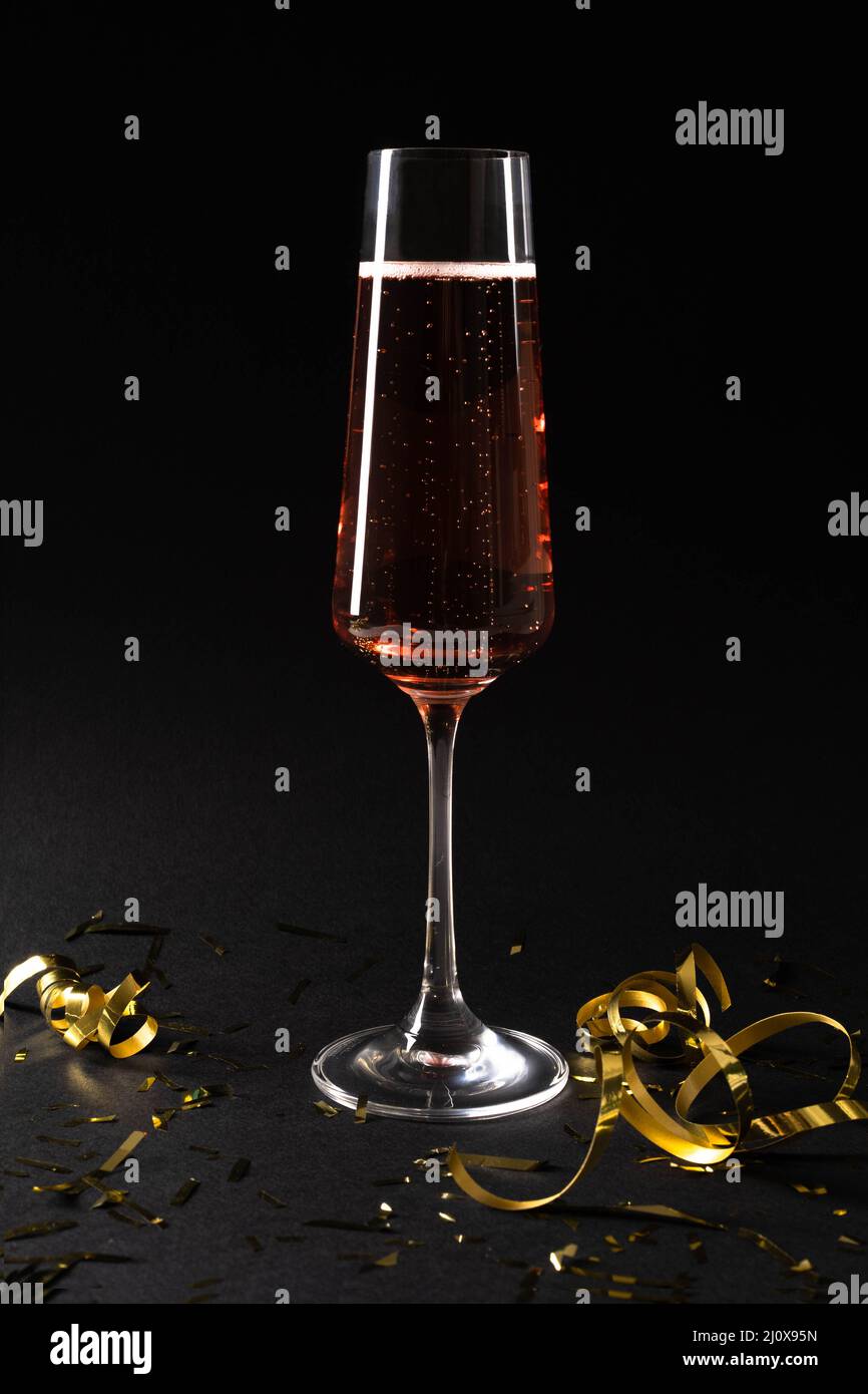 Una copa de vino espumoso champán sobre un fondo negro aislado. Lentejuelas doradas. El concepto de vacaciones, cumpleaños, vacaciones, boda, Navidad Foto de stock