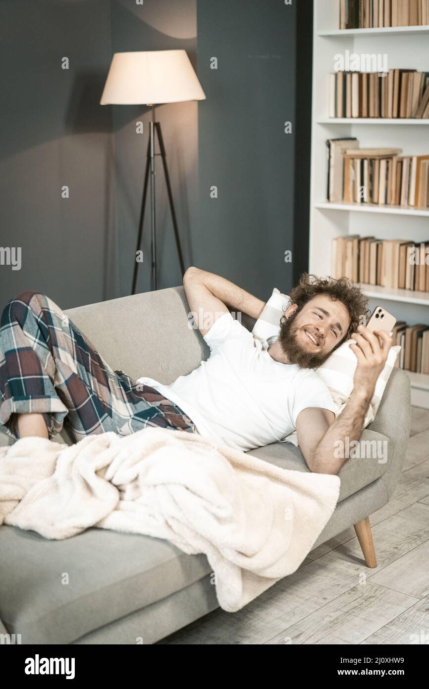 Hombre joven enfermo en pijamas durmiendo en el sofá mirando al smartphone  o teniendo videollamada . Hermoso hombre barbudo durmiendo Fotografía de  stock - Alamy