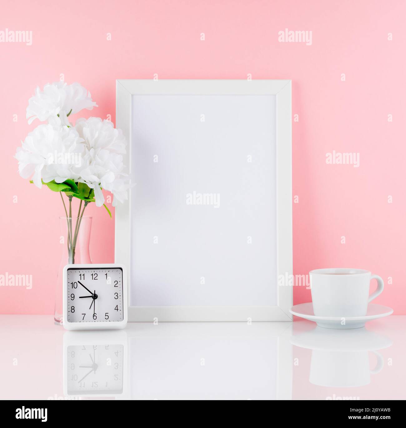 Marco blanco en blanco, flor, reloj, taza de café o té en una mesa blanca contra la pared rosa con espacio de copia. Se burlan. Foto de stock