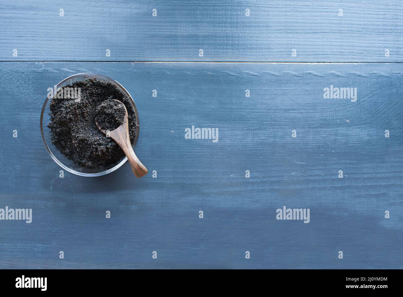 Vista de la mesa de los posos de café en un tazón de vidrio con cuchara de madera sobre un fondo de madera rústica azul oscuro. Forma orgánica sostenible de fertilizar Foto de stock