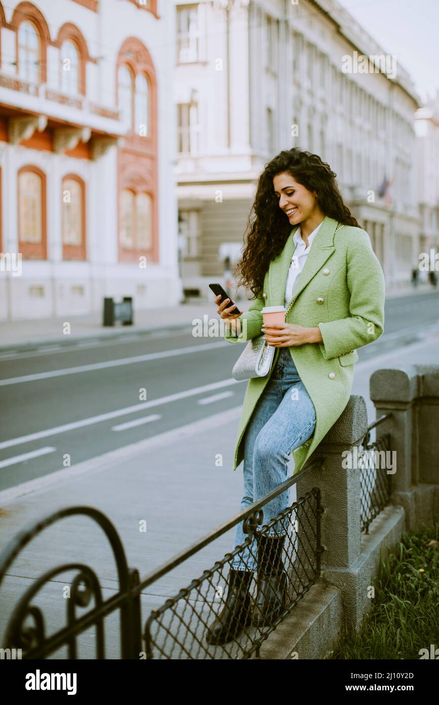 Una mujer joven con un smartphone en la calle y tomando café para llevar Foto de stock