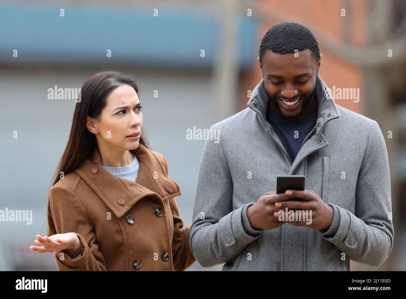 Hombre usando el teléfono inteligente ignorando a su enojado amigo caminando en la calle Foto de stock
