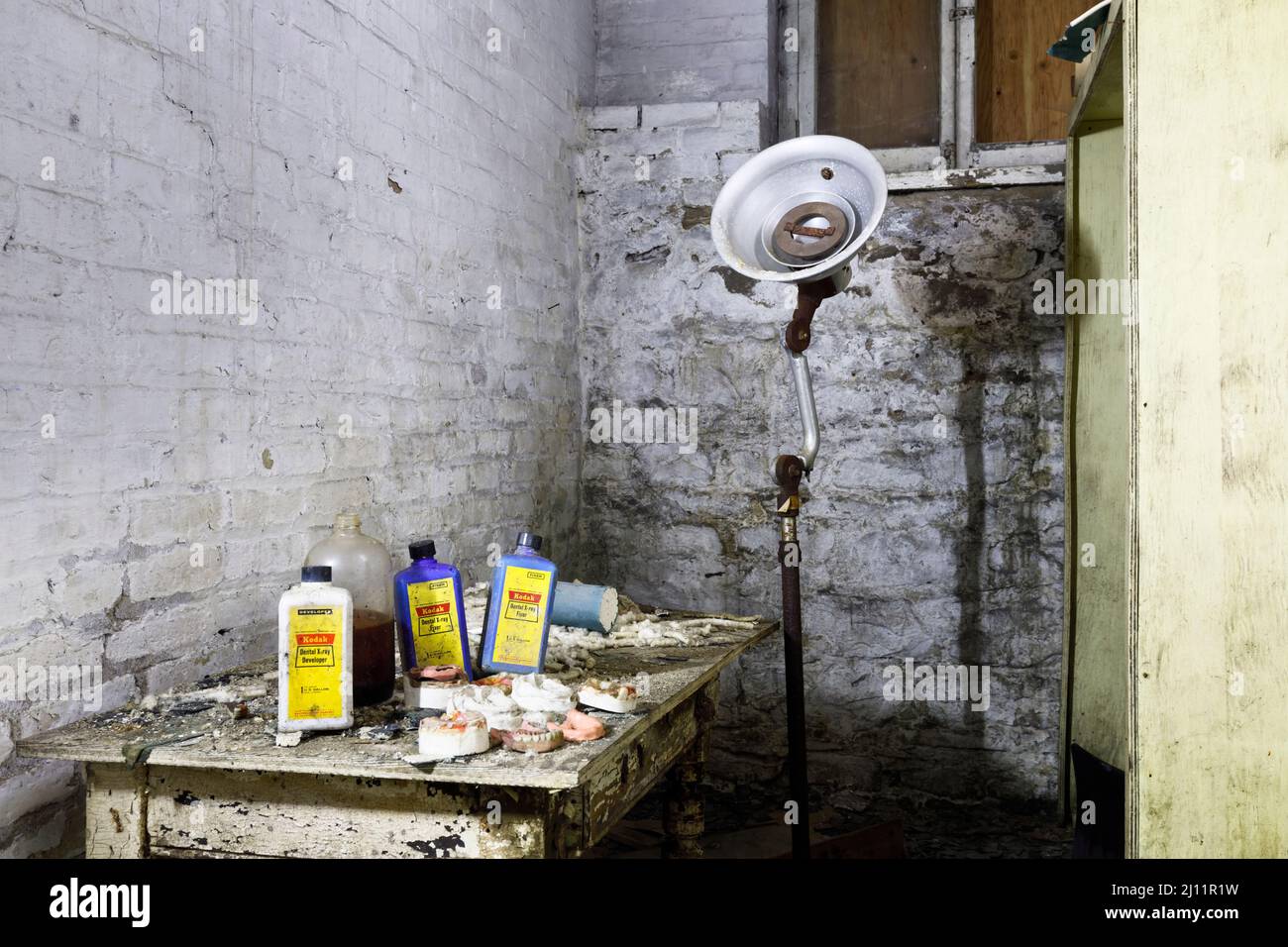 Moldes dentales, productos químicos de rayos X, dentaduras postizas y una vieja lámpara dental dentro del sótano de un asilo abandonado. Foto de stock