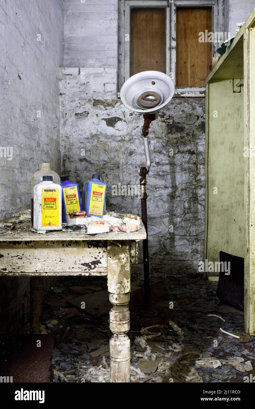 Moldes dentales, productos químicos de rayos X, dentaduras postizas y una vieja lámpara dental dentro del sótano de un asilo abandonado. Foto de stock