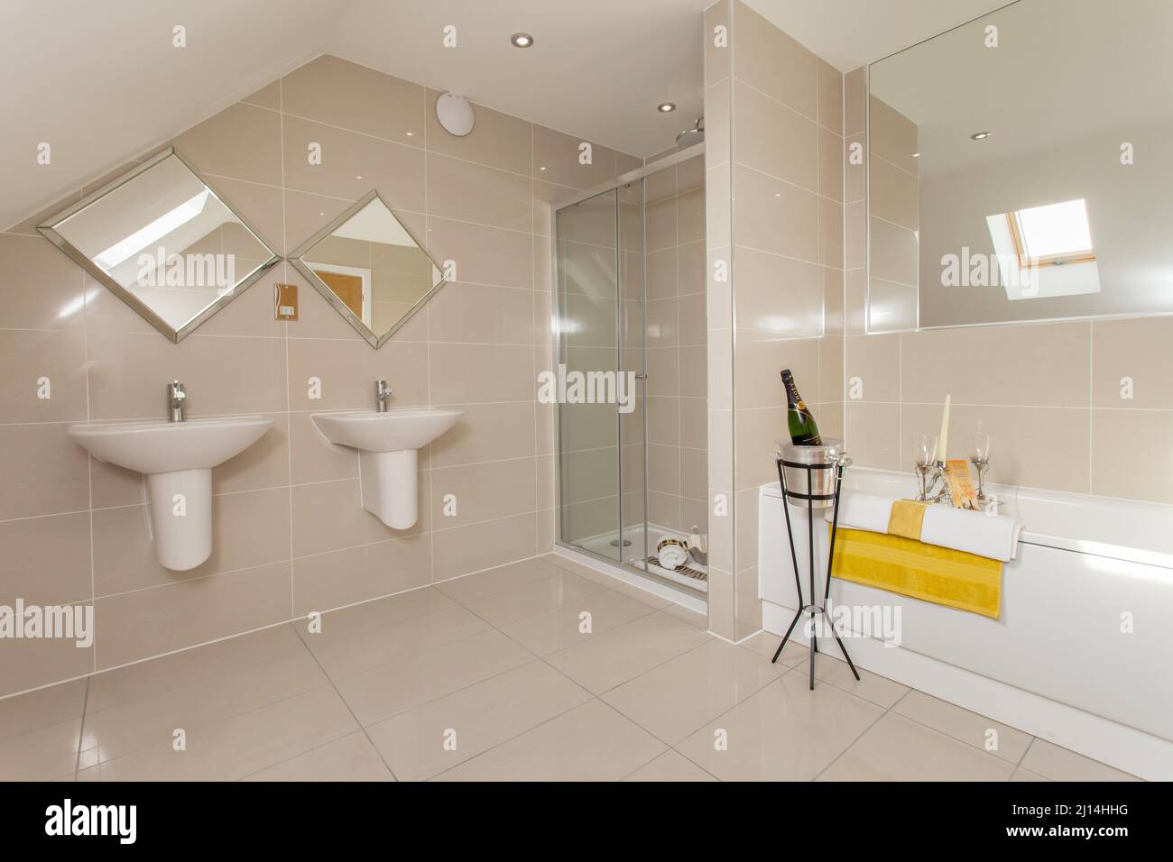 Champán al lado de la bañera en un moderno baño con inodoro, cabina de ducha, lavabos para él y ella, lavabos, azulejos en todo el hotel. Foto de stock
