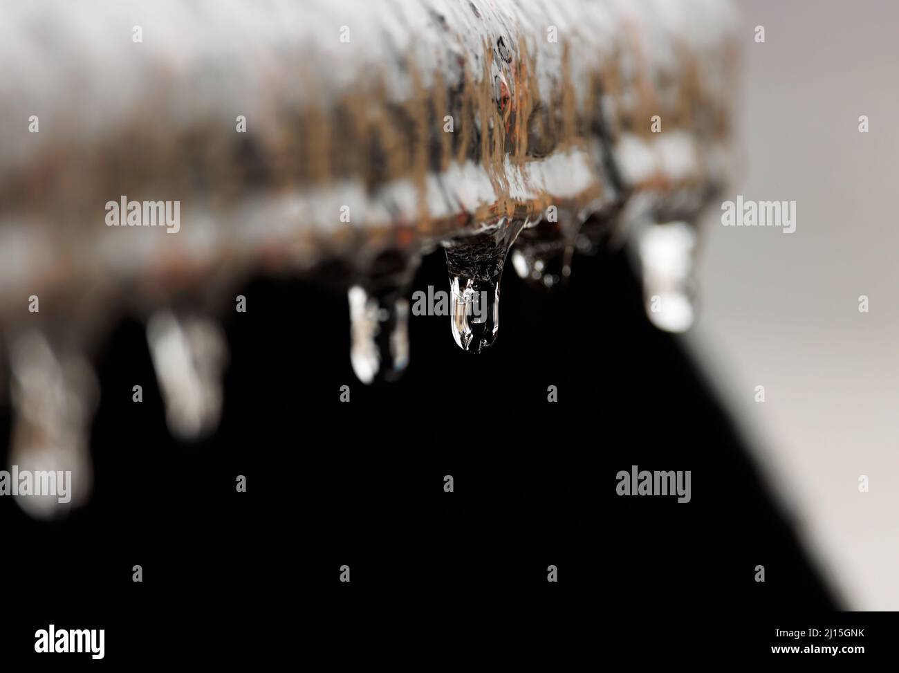 el agua congelada cae colgando de un saliente de metal oxidado con una profundidad de campo poco profunda Foto de stock