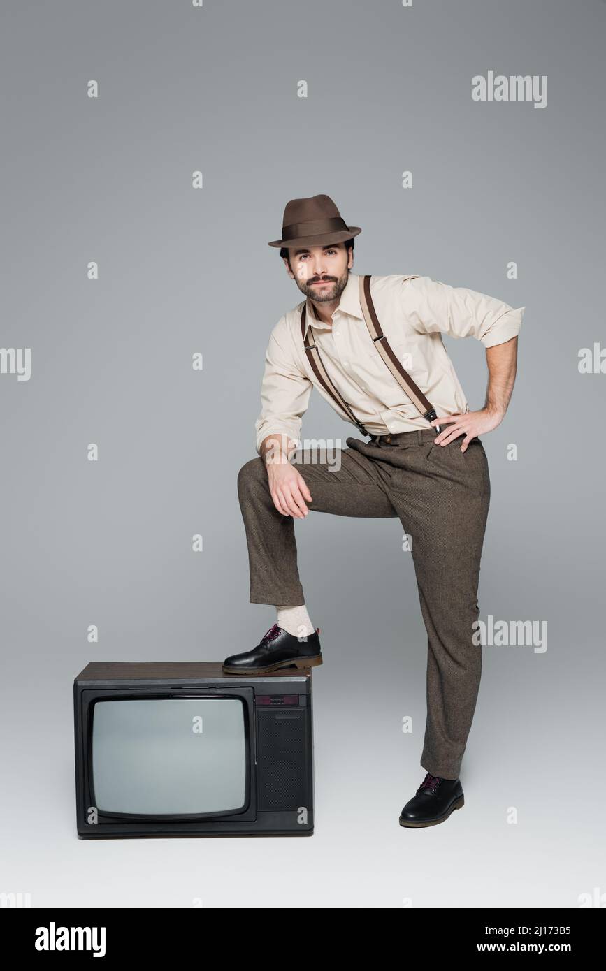 ropa de hombre estilo vintage posando con la mano en la cadera cerca de la  televisión antigua en gris Fotografía de stock - Alamy