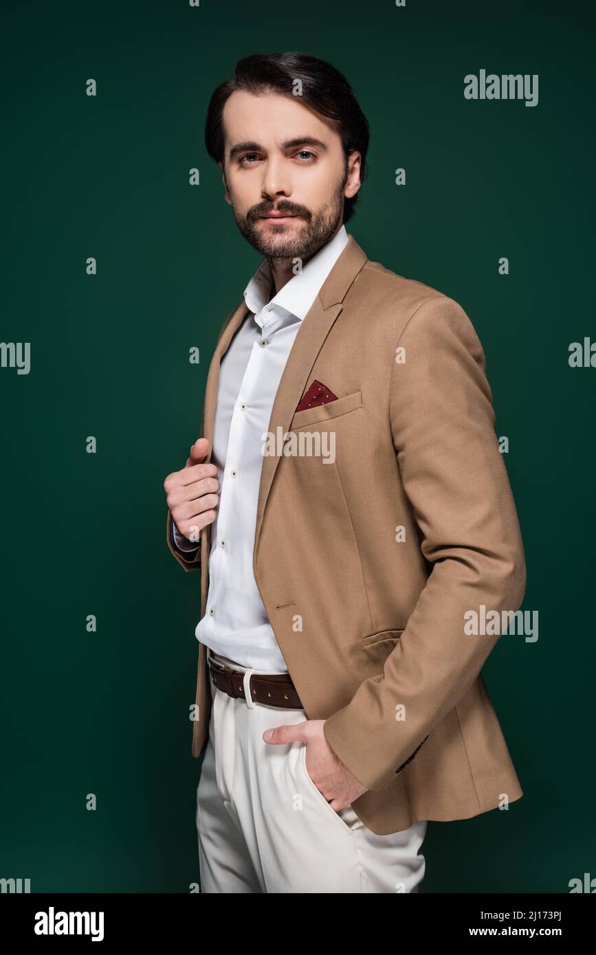 hombre en color beige blazer mirando a la cámara y de pie con la mano en el  bolsillo sobre verde oscuro Fotografía de stock - Alamy
