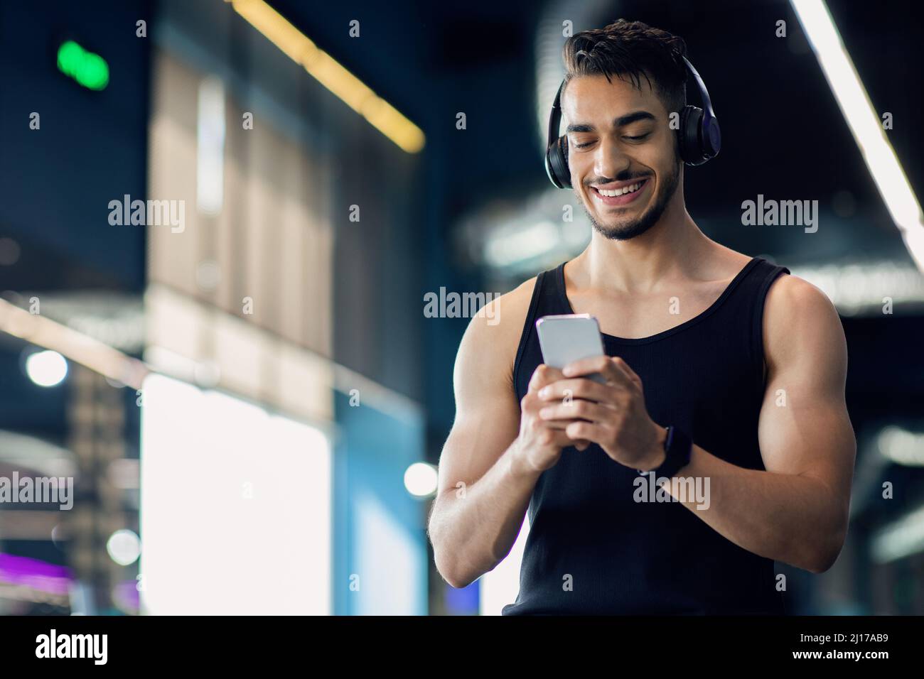 Atleta masculino de Oriente Medio en auriculares inalámbricos utilizando el  teléfono móvil en el gimnasio Fotografía de stock - Alamy