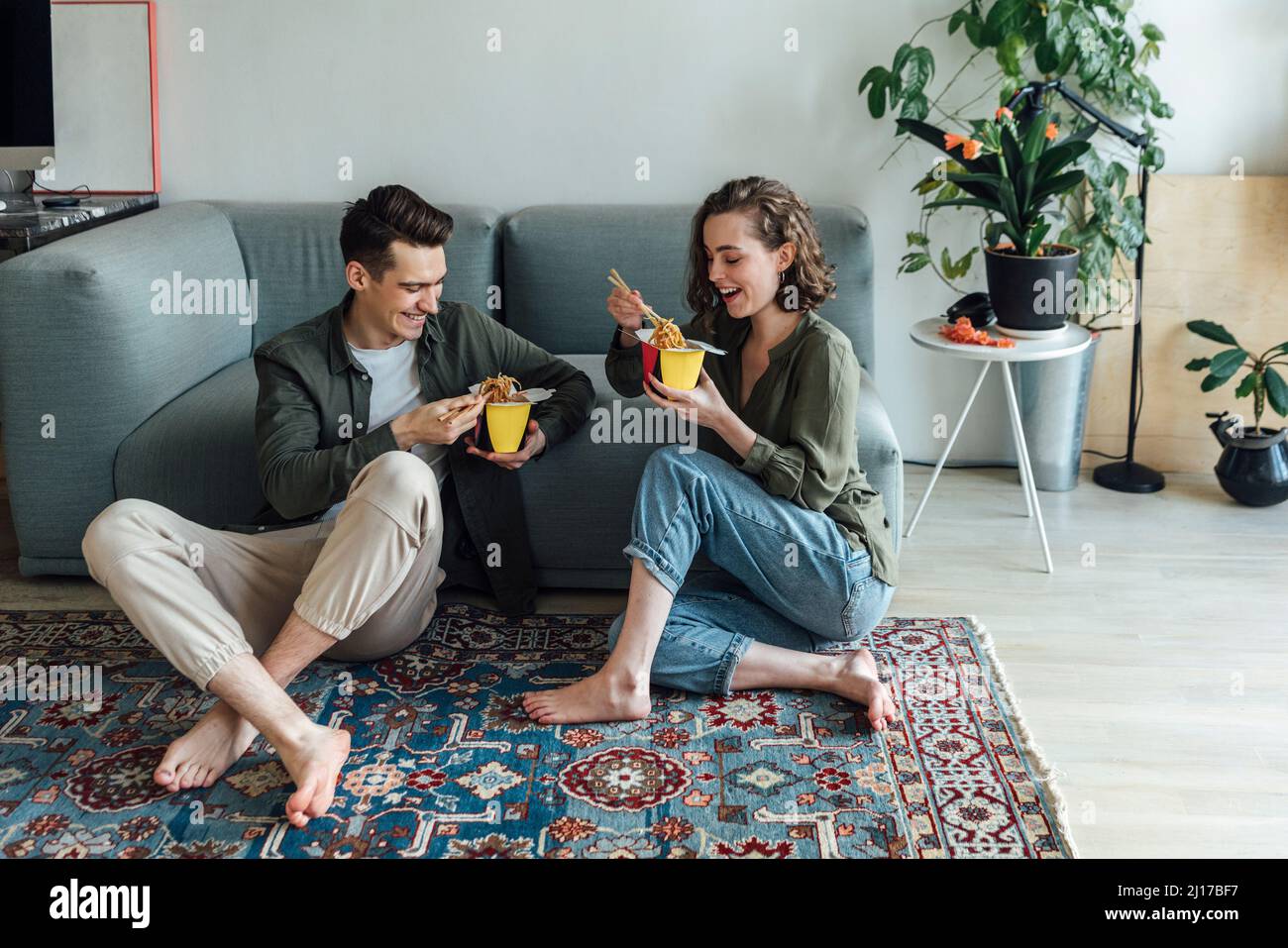 Feliz pareja joven con comida para llevar sentado junto al sofá en la sala de estar en casa Foto de stock