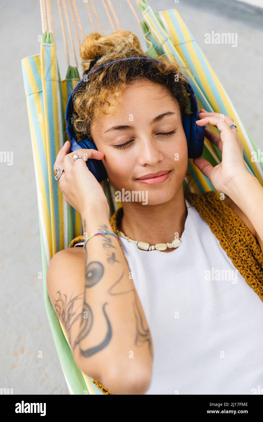 Hermosa mujer con los ojos cerrados escuchando música a través de los auriculares en la hamaca Foto de stock