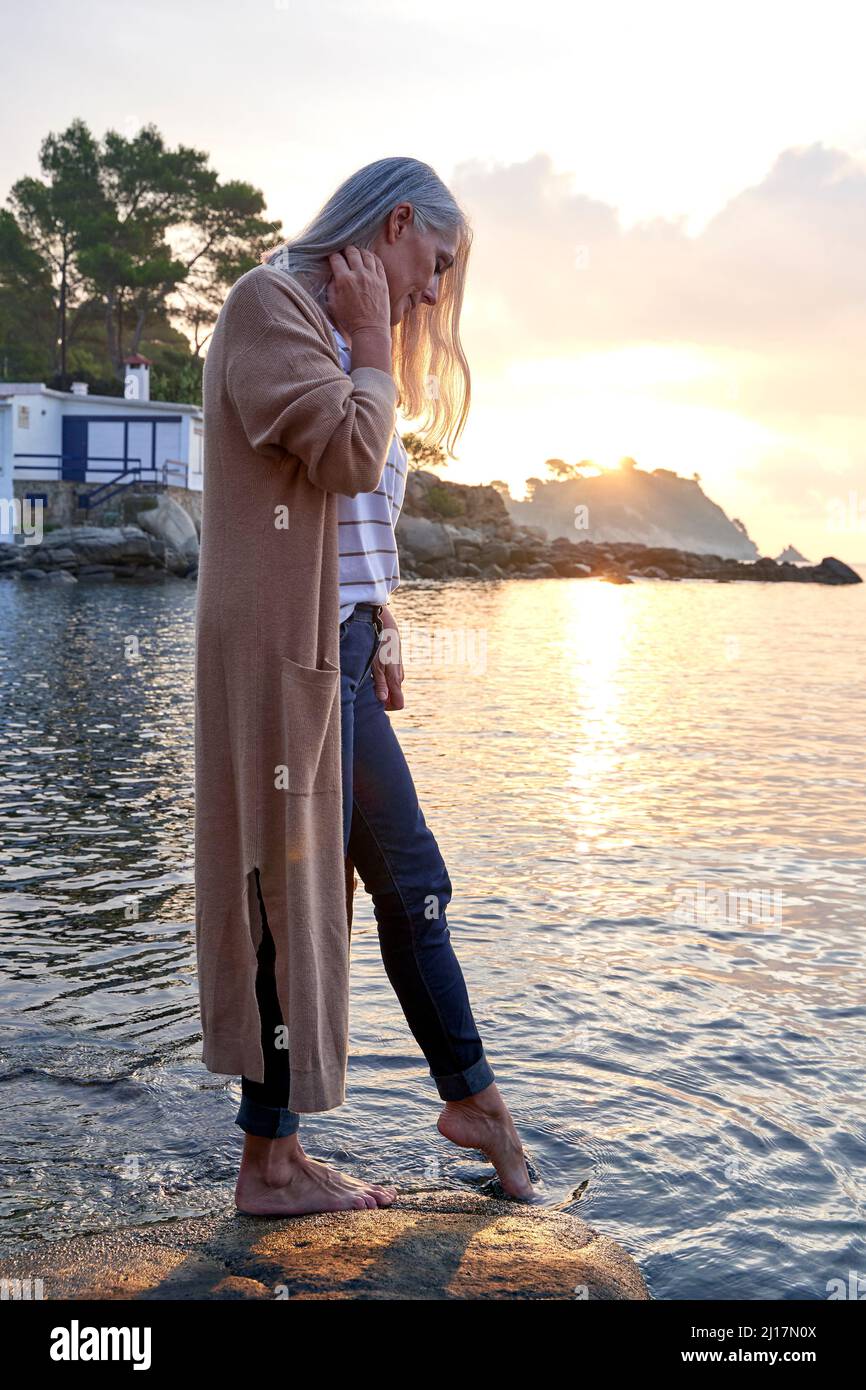 Mujer sumergiendo pie en el agua de pie sobre la roca en la playa Foto de stock