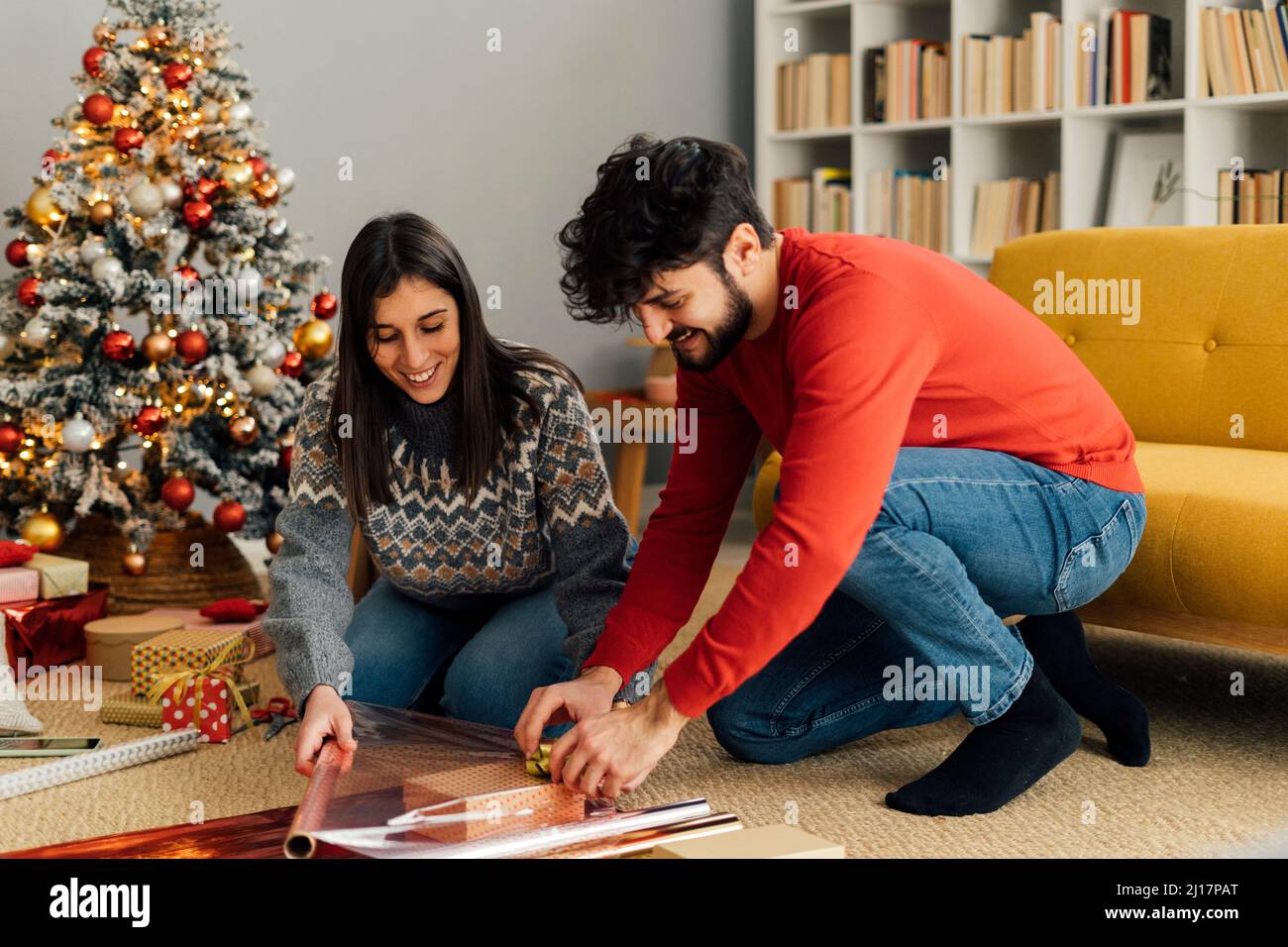 Pareja sonriente envolver regalo de Navidad en la sala de estar en casa Foto de stock
