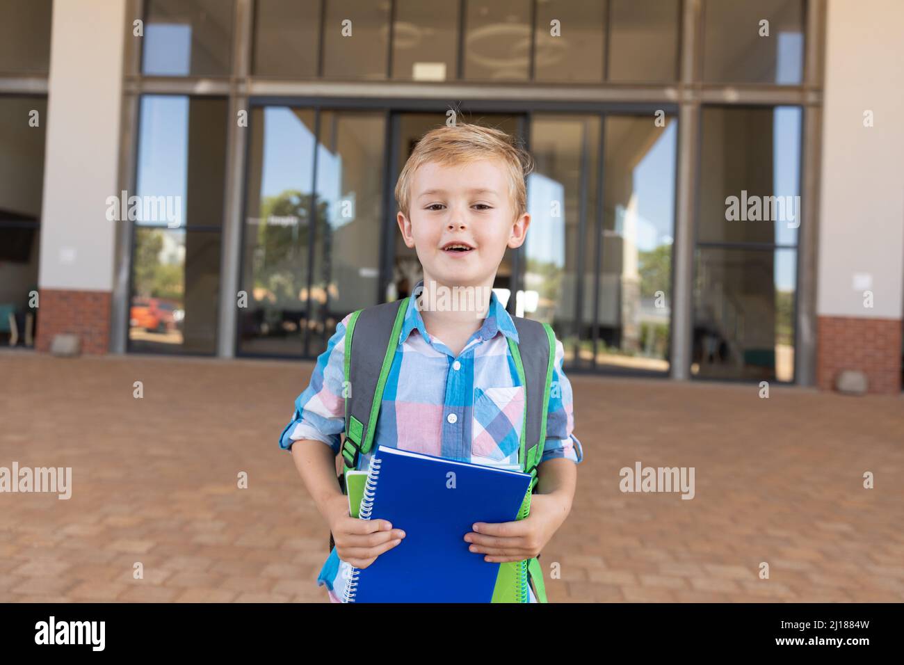 Retrato de un lindo y sonriente estudiante de escuela primaria caucásica con libros de pie en el campus de la escuela Foto de stock
