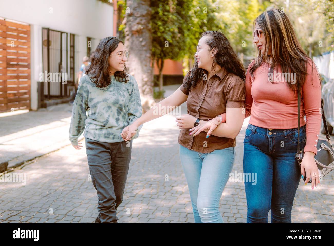 Tres mujeres jóvenes caminan por la calle, están sonriendo, jugando y pasándose bien. Foto de stock
