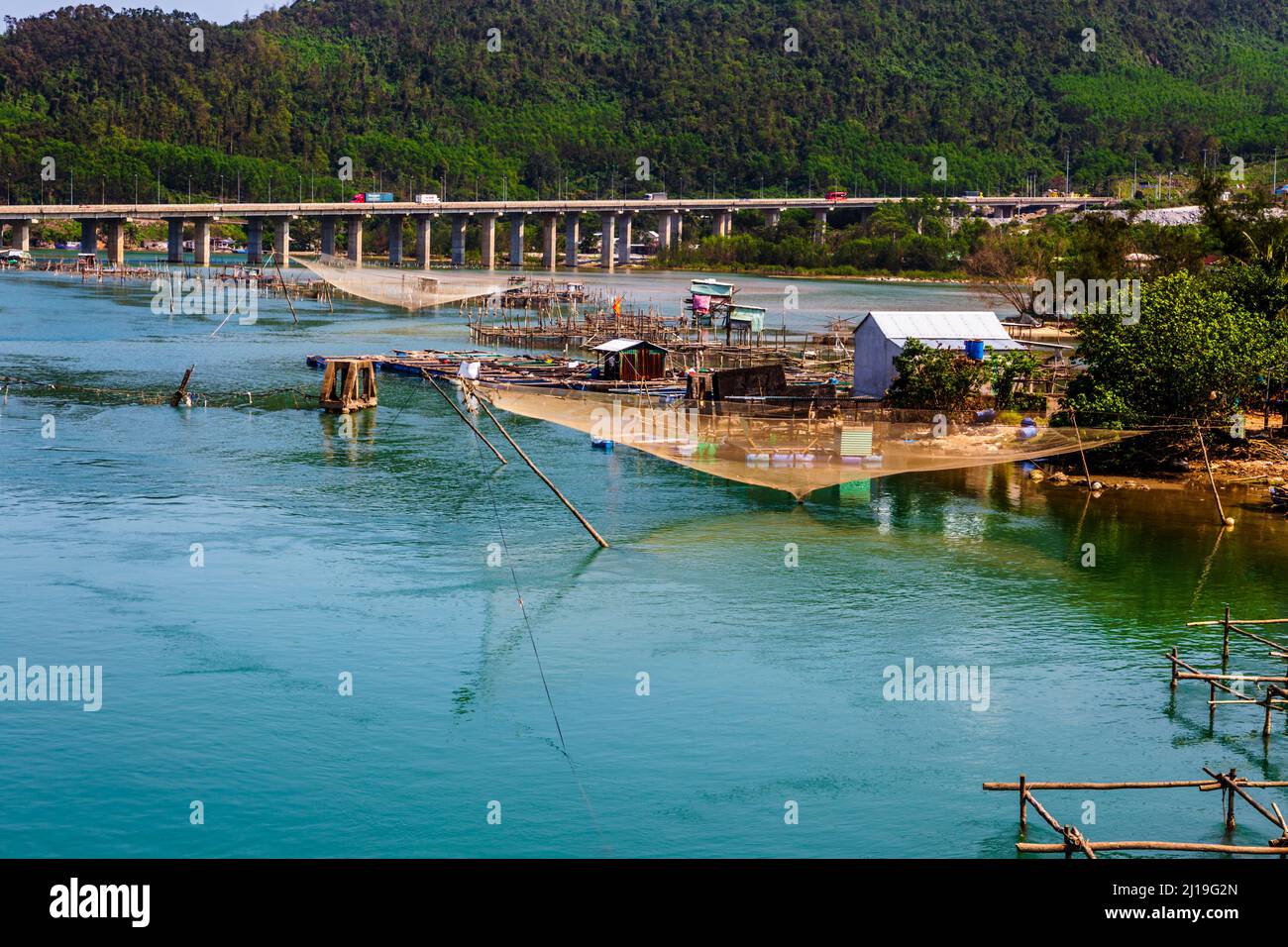 Un pequeño pueblo pesquero Lang Co ensenada entre varios puentes de carretera. Una gran red de pesca de color naranja sobre agua de color aguamarina. Foto de stock