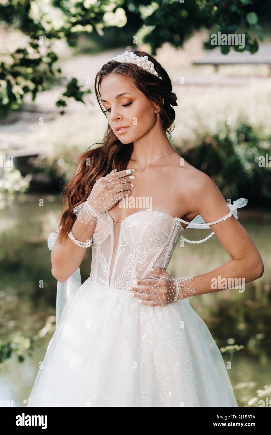 Una elegante novia con un vestido blanco, guantes con un ramo en una  cascada en el Parque, disfrutando de la naturaleza.Modelo en un vestido de  boda y guantes en el bosque Fotografía