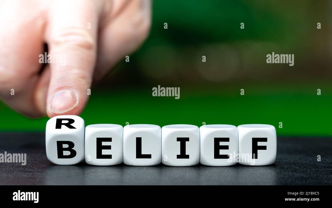 Símbolo para encontrar alivio a través de la religión. La mano da vuelta a los dados y cambia la palabra creencia a alivio. Foto de stock