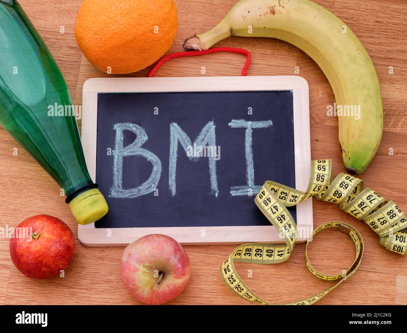 La abreviatura IMC (índice de masa corporal) en una pizarra y algunas frutas, una botella de agua y cinta métrica alrededor de ella. Primer plano. Foto de stock