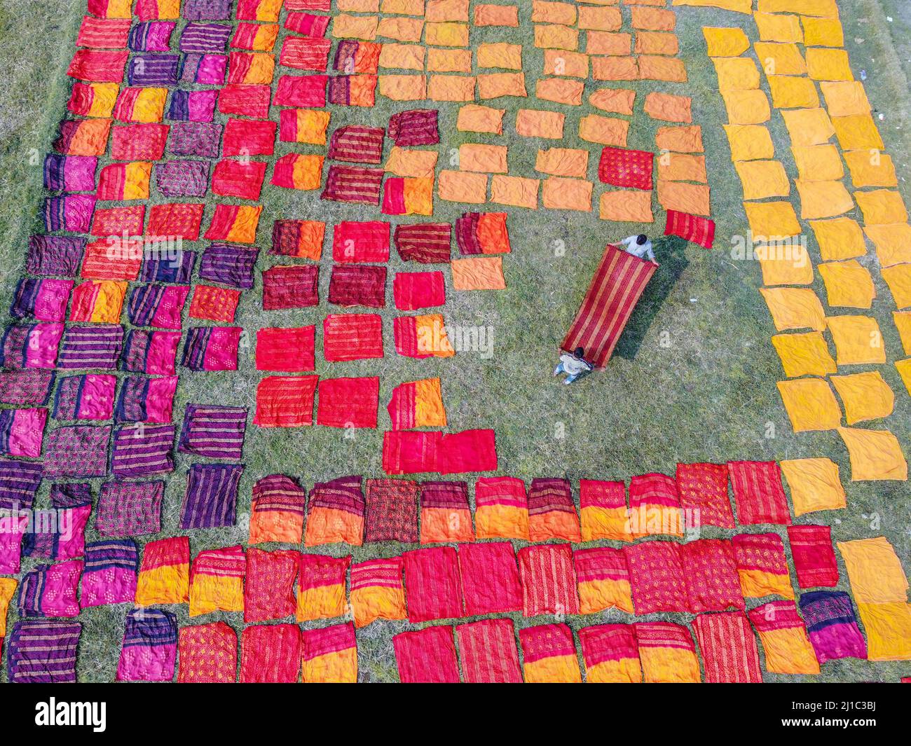 Narayanganj, Dhaka, Bangladesh. 24th Mar, 2022. Miles de paños de colores se ponen para secar bajo el sol caliente. Una vez teñida la tela, se extiende sobre un campo, que cubre aproximadamente 10.000 pies cuadrados, en la aldea de Batik en Narayanganj, Bangladesh. Una vez que están secos - que normalmente toma cuatro horas - se hacen en la ropa que se venden en todo el mundo. (Imagen de crédito: © Mustasinur Rahman Alvi/ZUMA Press Wire) Foto de stock