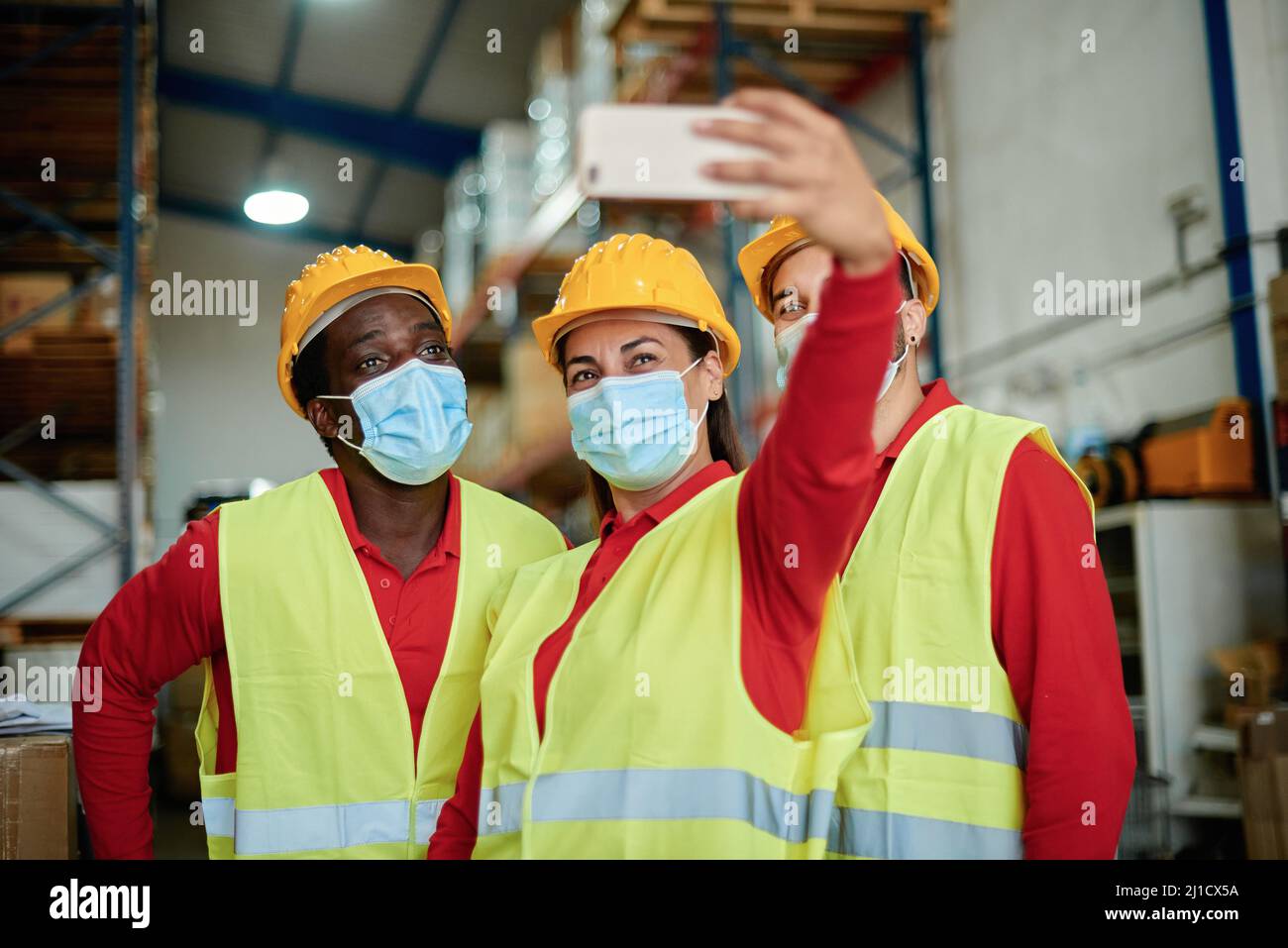 Felices trabajadores multirraciales tomando una selfie dentro de la ropa de seguridad del almacén - Enfoque en la cara de la mujer. Foto de stock