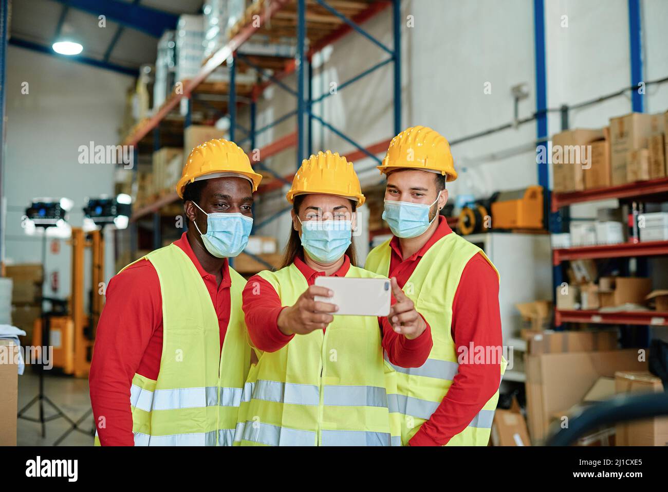 Felices trabajadores multirraciales tomando una selfie dentro de la ropa de seguridad del almacén - Enfoque en la cara de la mujer. Foto de stock