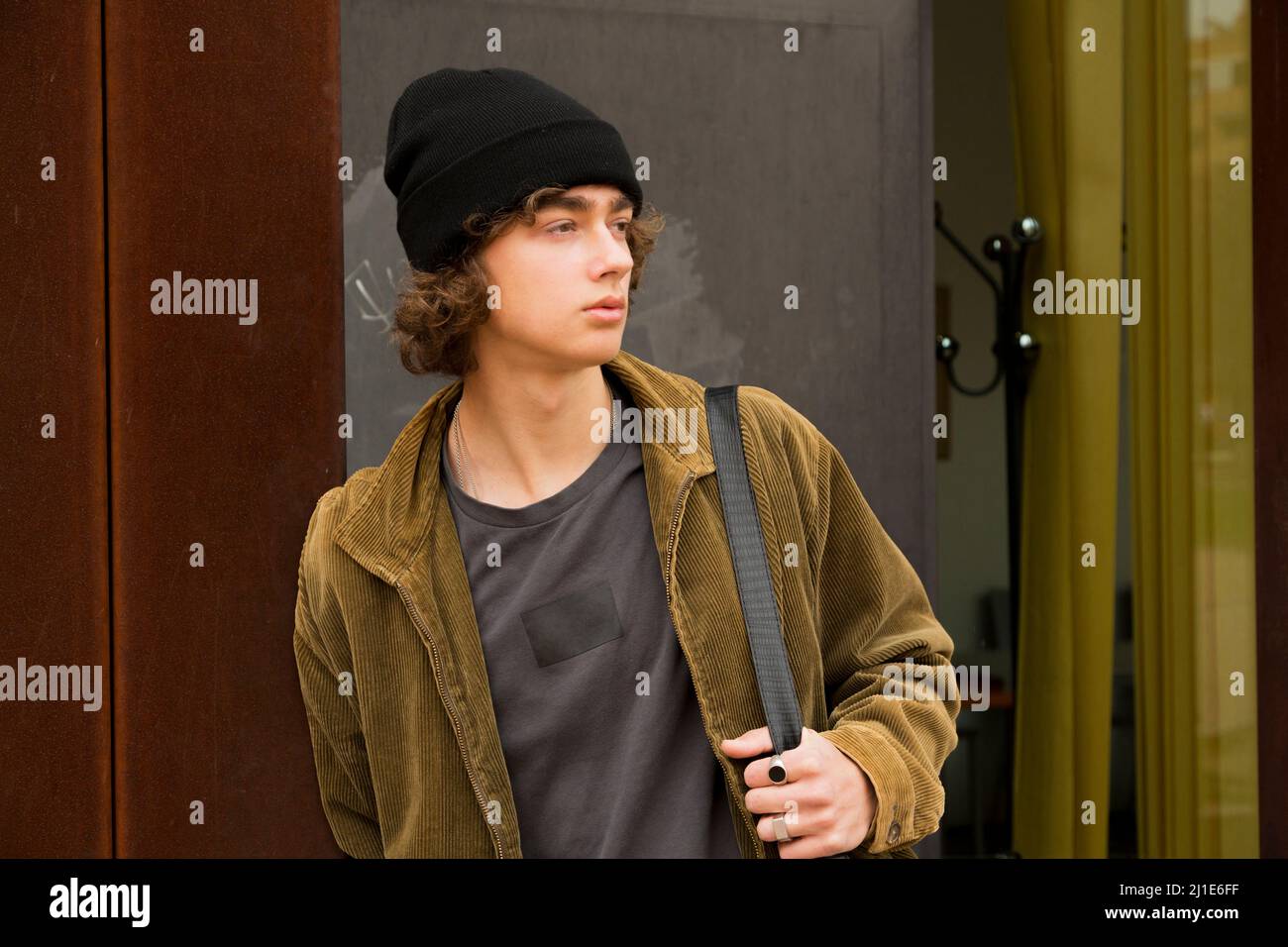 retrato hombre joven con pelo rizado y gorra de lana con maletín inclinado  contra la pared esperando mirando hacia los lados Fotografía de stock -  Alamy