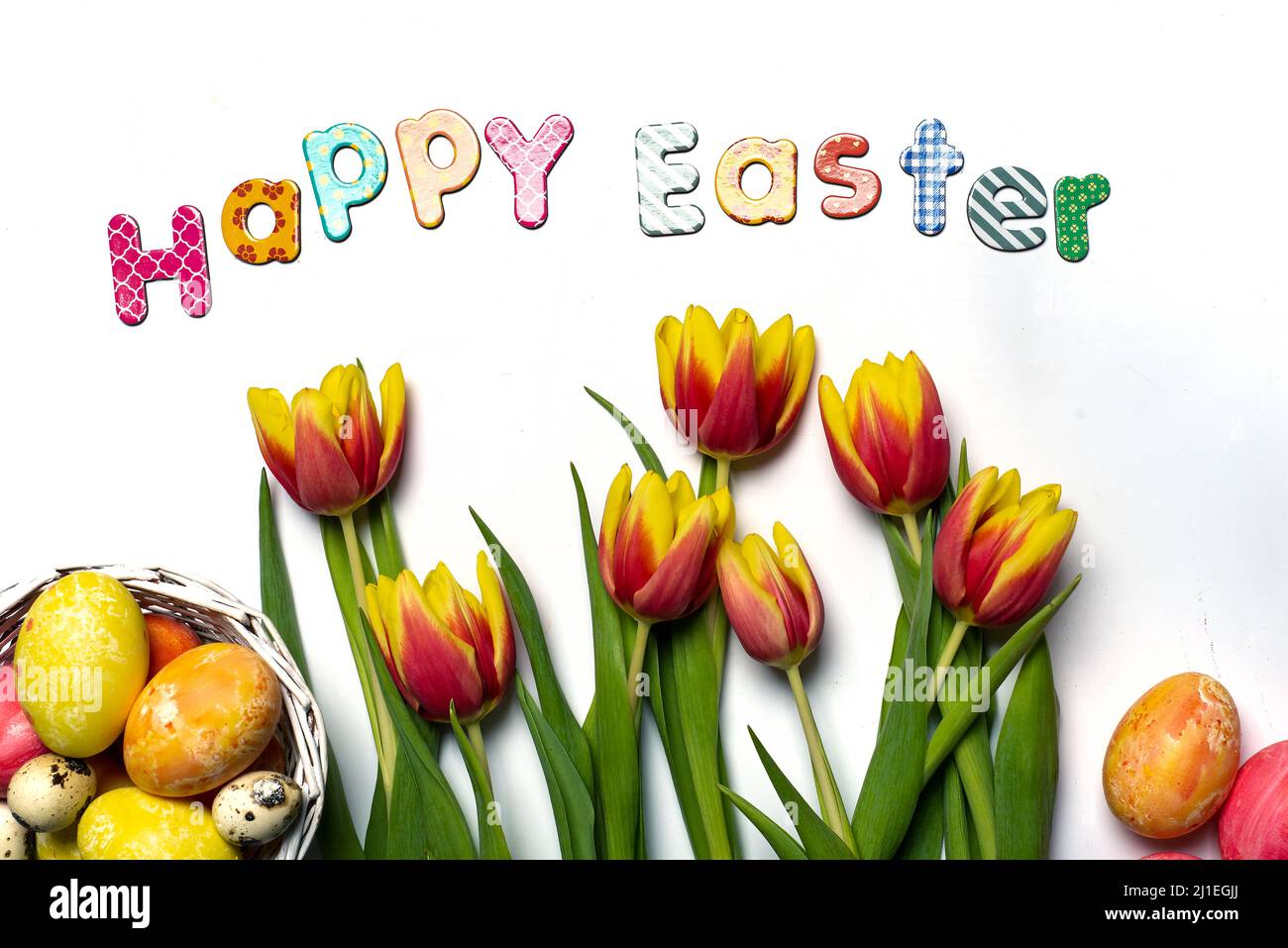 Feliz tarjeta de Pascua con huevos de Pascua pintados de rojo y amarillo dos flores de tulipán de color sobre fondo blanco vista superior plana lay Foto de stock