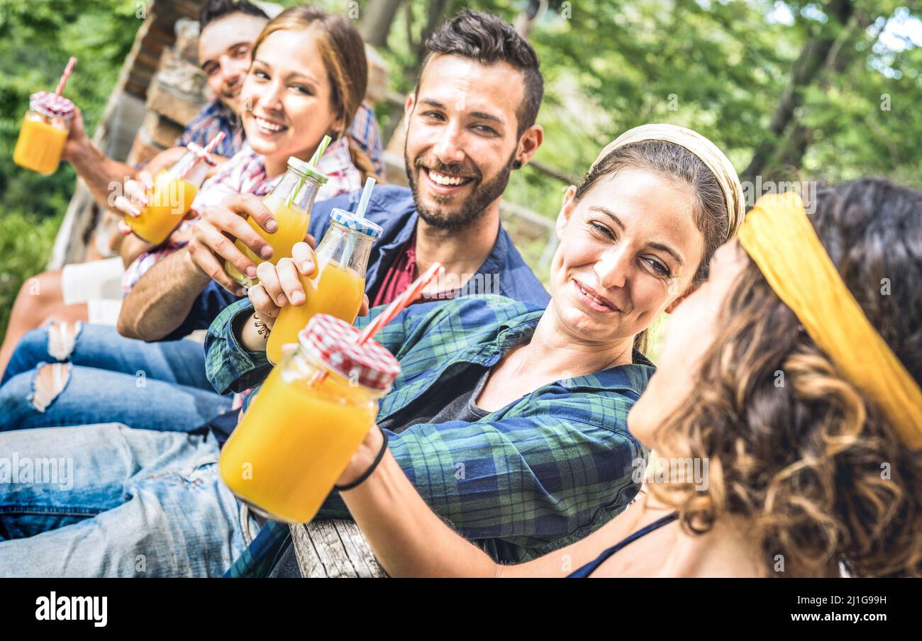 Amigos felices bebiendo jugo de fruta naranja saludable en el campo picnic - Jóvenes milenios Diviértete juntos al aire libre en la merienda de la tarde en Foto de stock