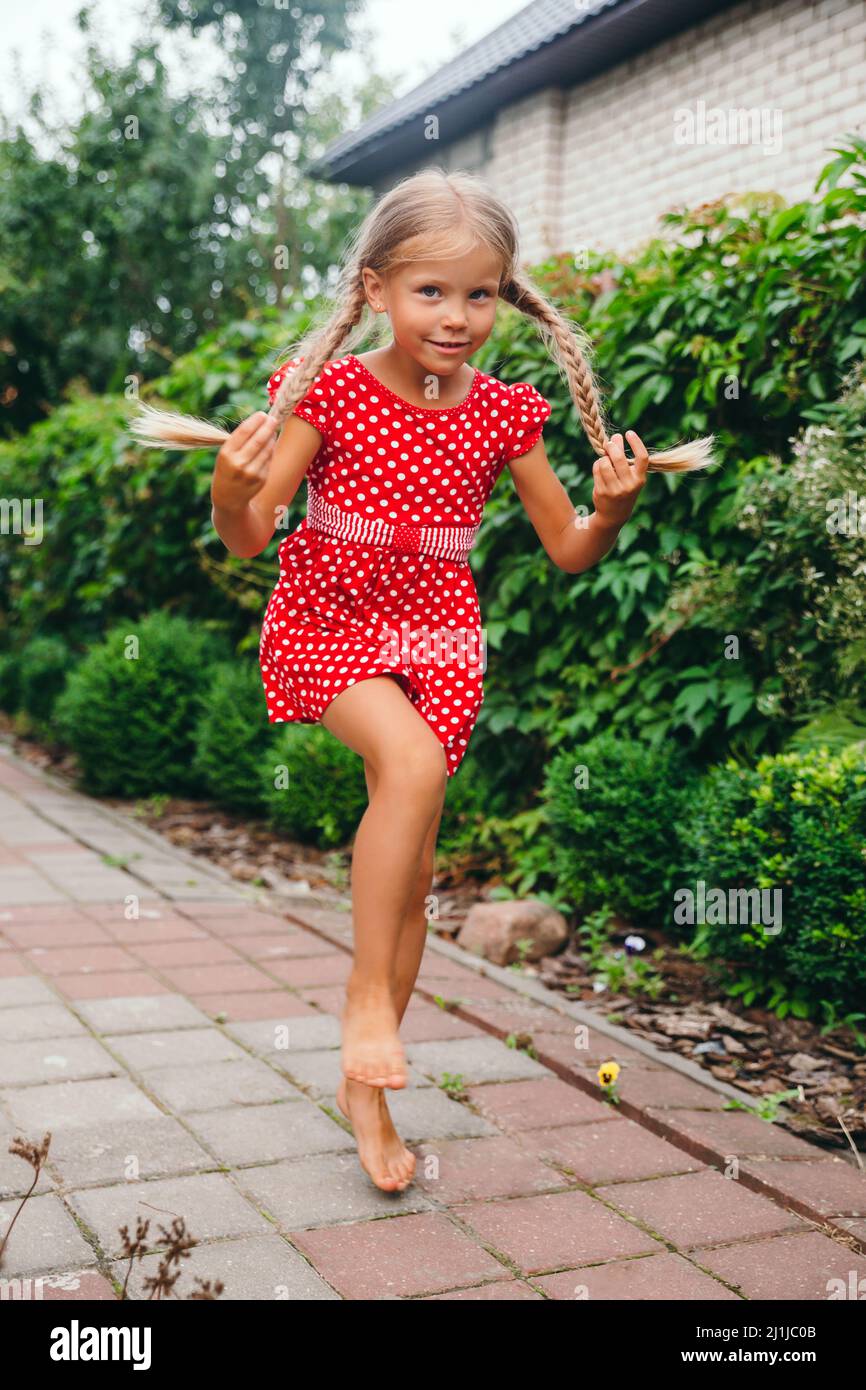 Feliz niña de 3 años en vestido rojo está jugando en el jardín de verano de  la aldea