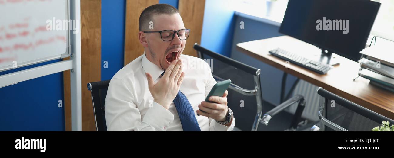 Un hombre en la oficina grina en su lugar de trabajo. Dilación. Foto de stock