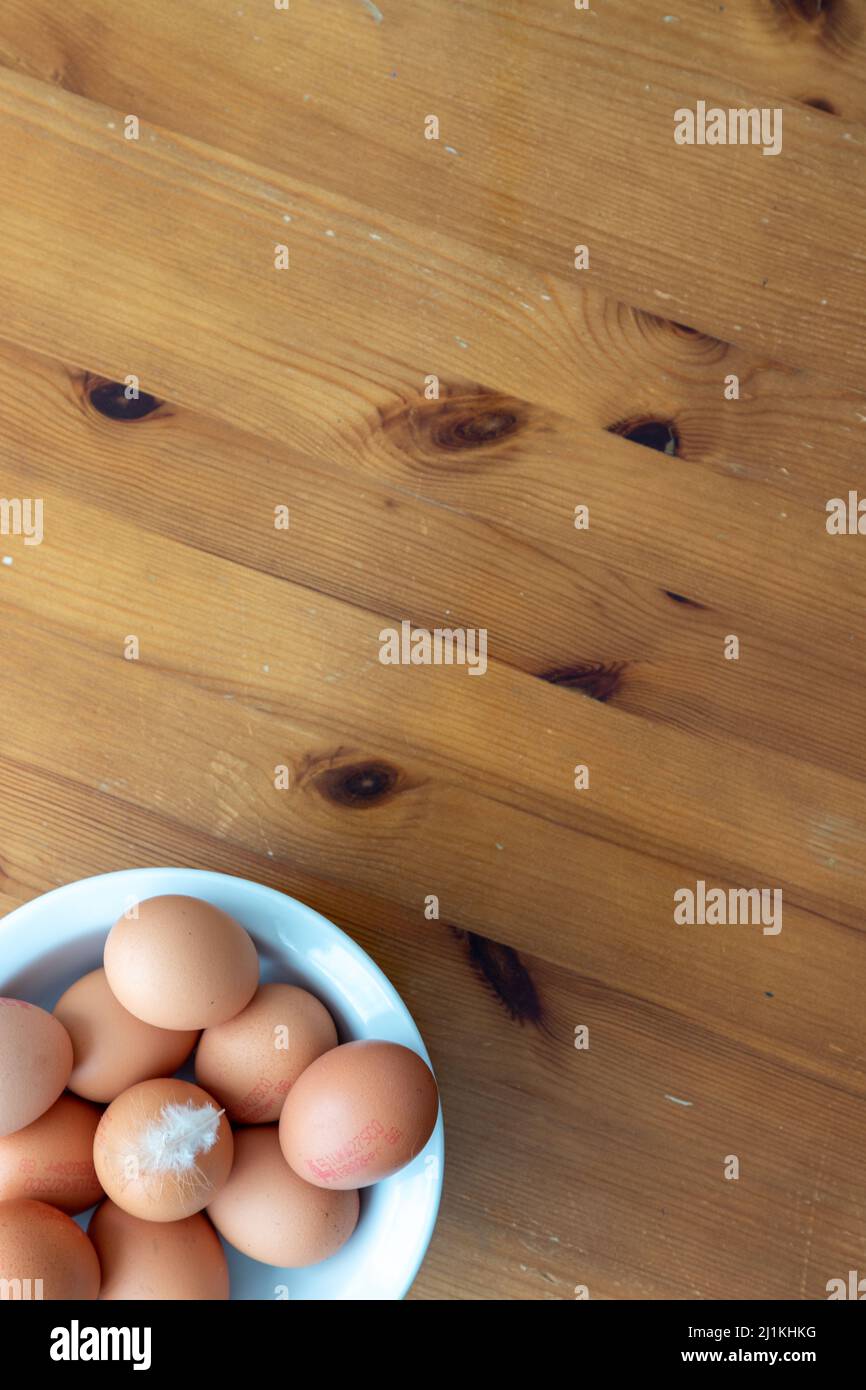 Una imagen plana de un cuenco de huevos sobre un fondo de madera con una pluma en la parte superior del huevo Foto de stock