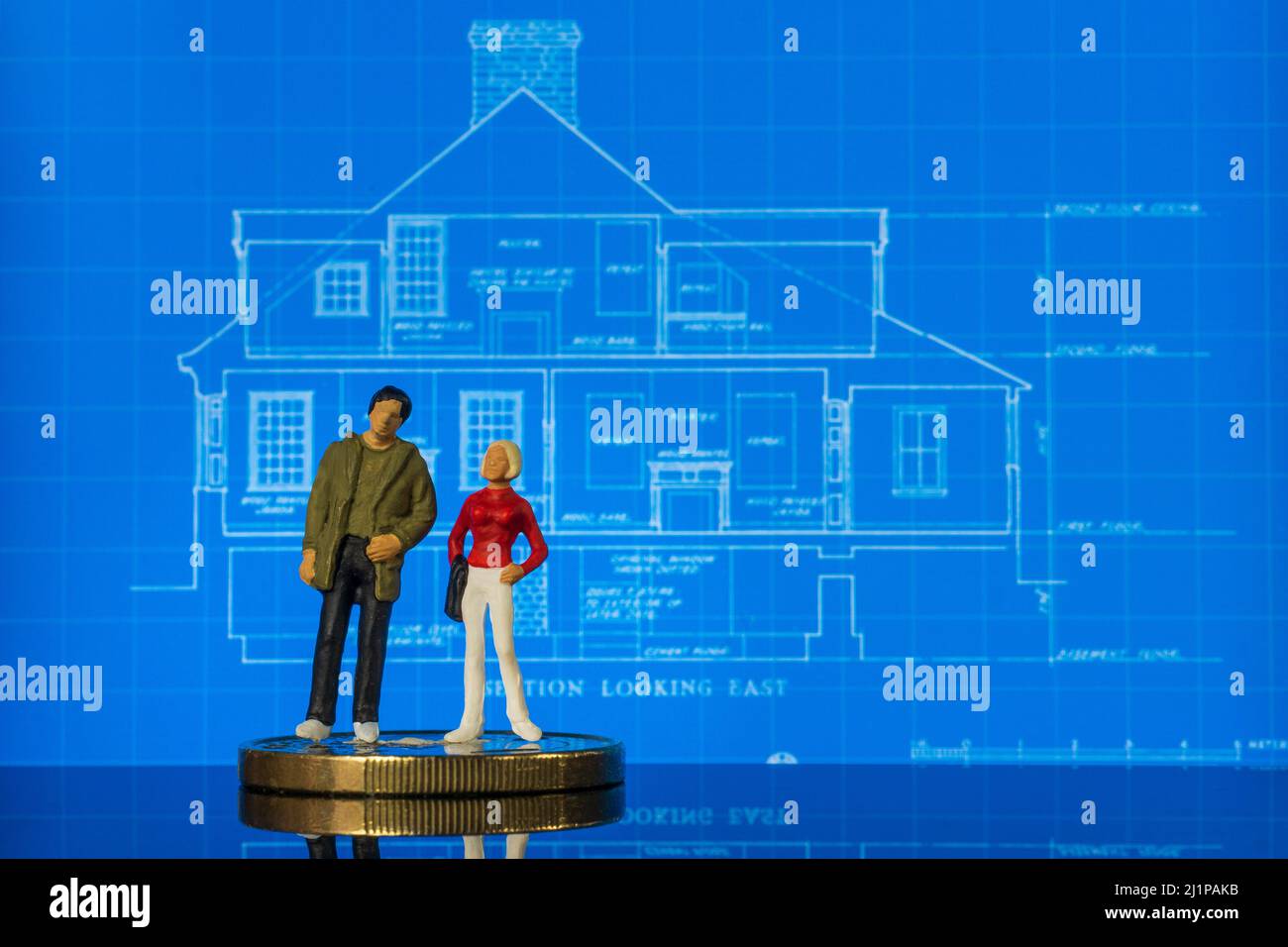 Dos figuras en miniatura de pie en un plano de la casa como si se discutieran los planes Foto de stock