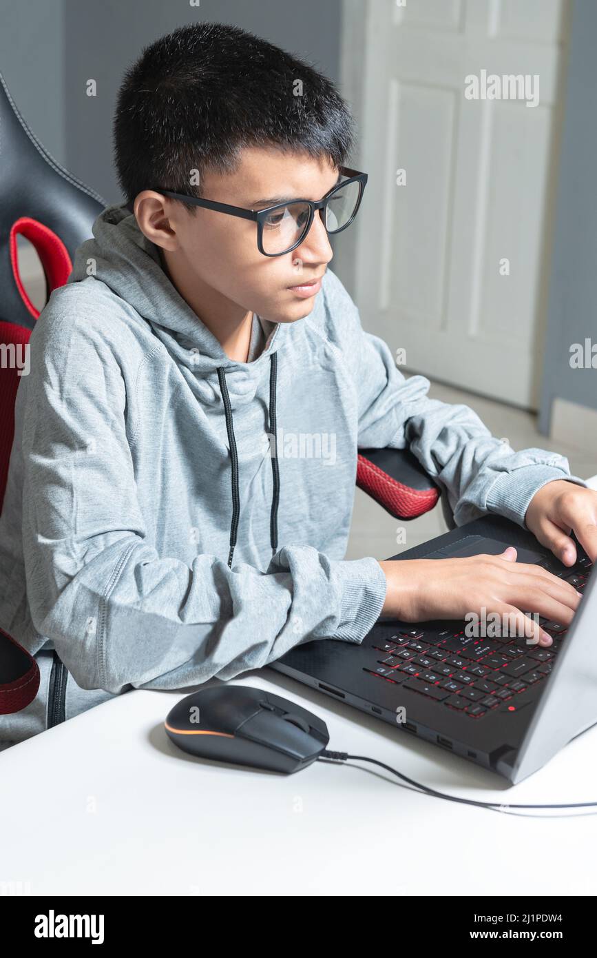 Adolescente niño en casa escuela estudio sala escritorio pc gafas de ordenador sentado mirando la tarea Foto de stock