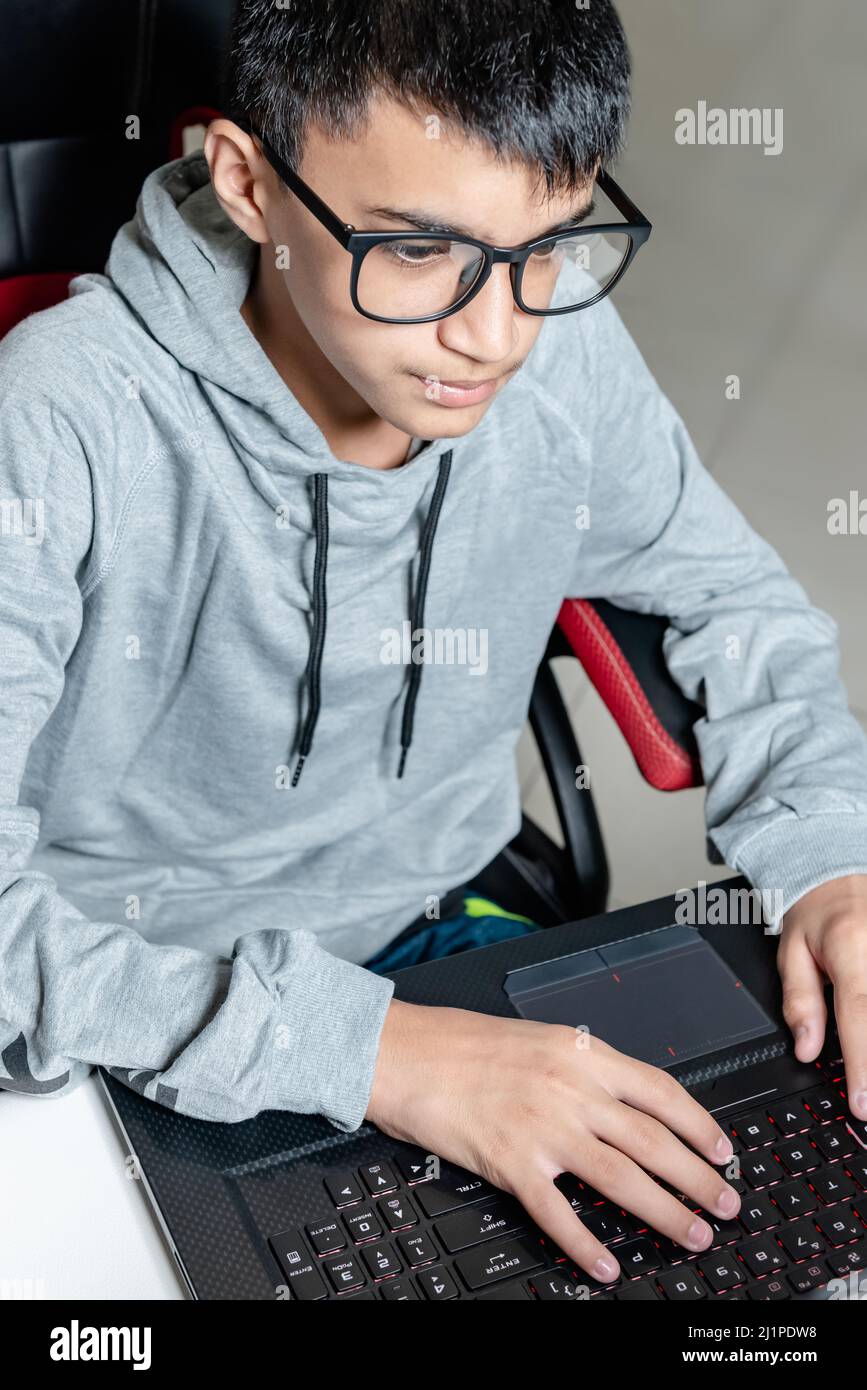 Adolescente niño en casa escuela estudio sala escritorio pc gafas de ordenador sentado mirando la tarea Foto de stock