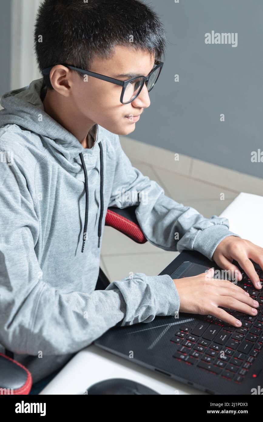 Adolescente niño en casa escuela estudio sala escritorio PC gafas de ordenador sentado mirando la tarea Foto de stock