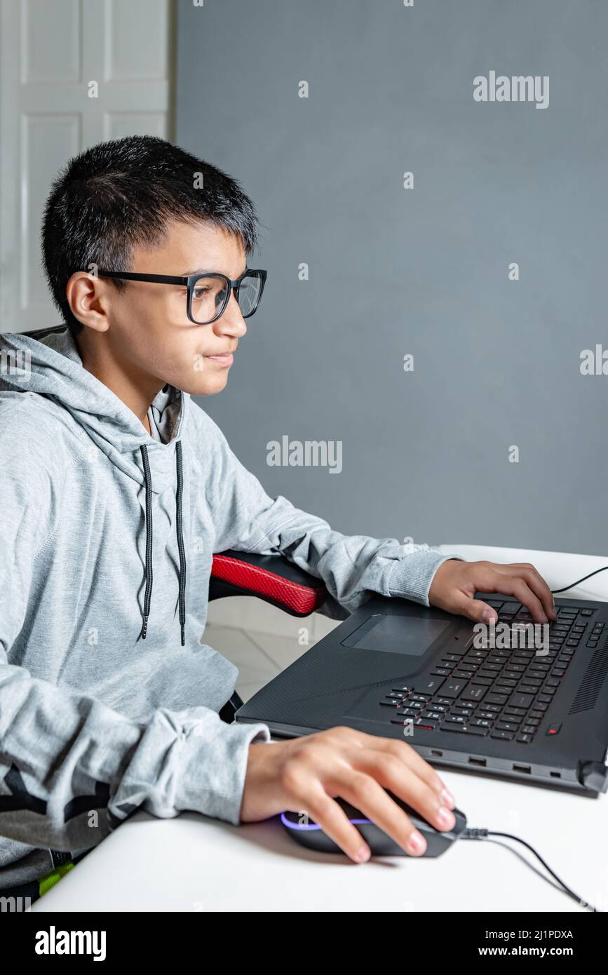 Adolescente niño en casa escuela estudio sala escritorio PC gafas de ordenador sentado mirando la tarea Foto de stock