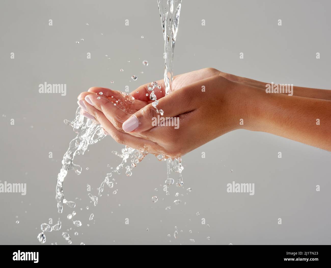 Pureza en la palma de sus manos. Foto recortada de las manos sujetada bajo una corriente de agua sobre un fondo gris. Foto de stock