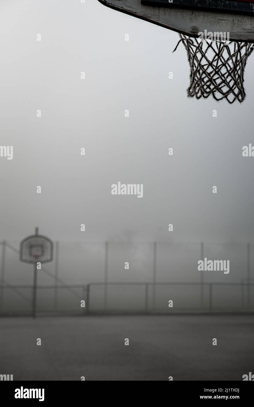 La cancha de baloncesto de la calle en la niebla transmite tristeza y vacío. El campo de baloncesto abandonado proporciona una ilustración de la guerra, la fuga y el vuelo desde casa Foto de stock