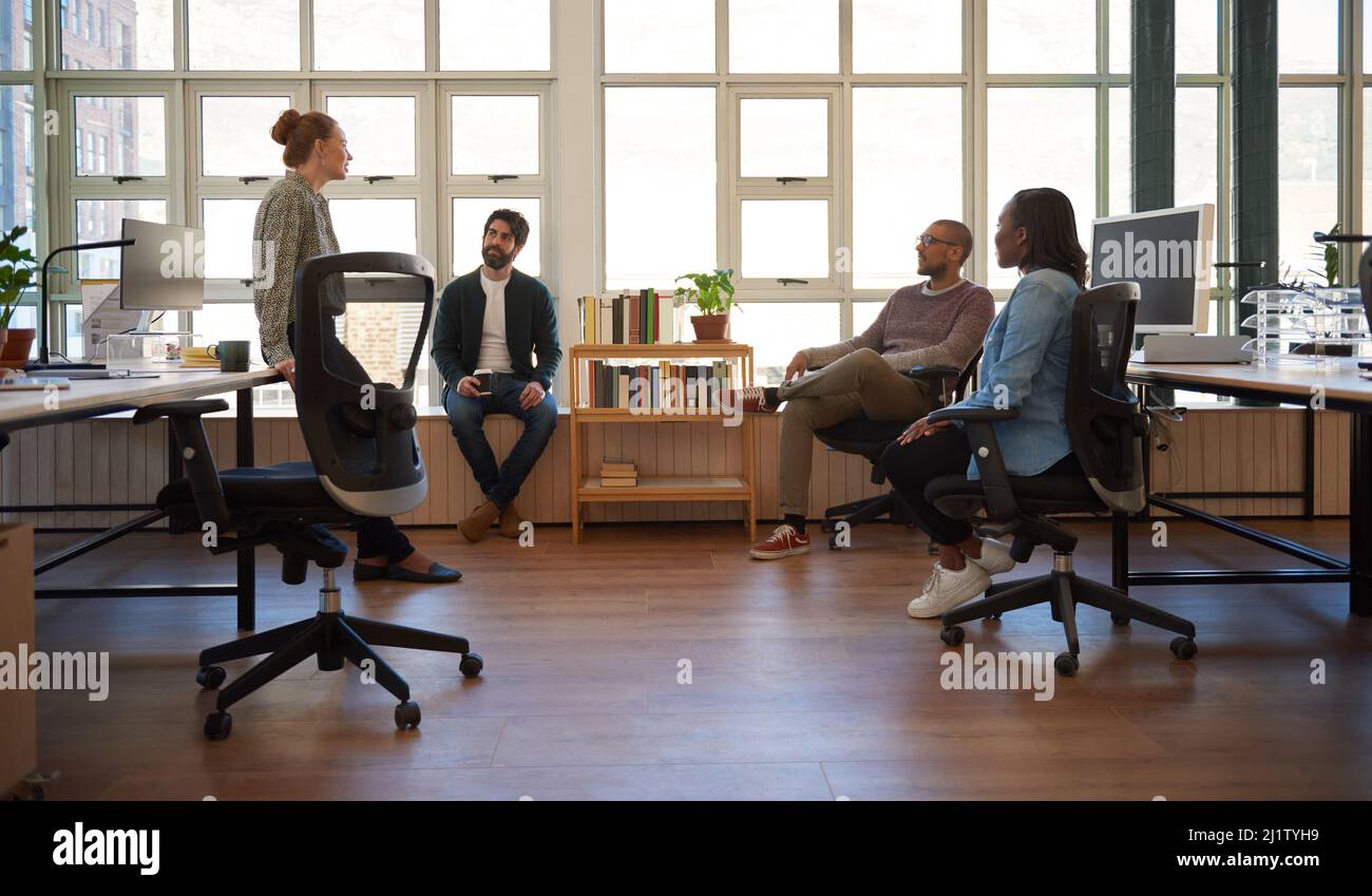 Joven empresaria hablando con un grupo de diversos colegas durante una reunión informal en una oficina moderna y luminosa Foto de stock
