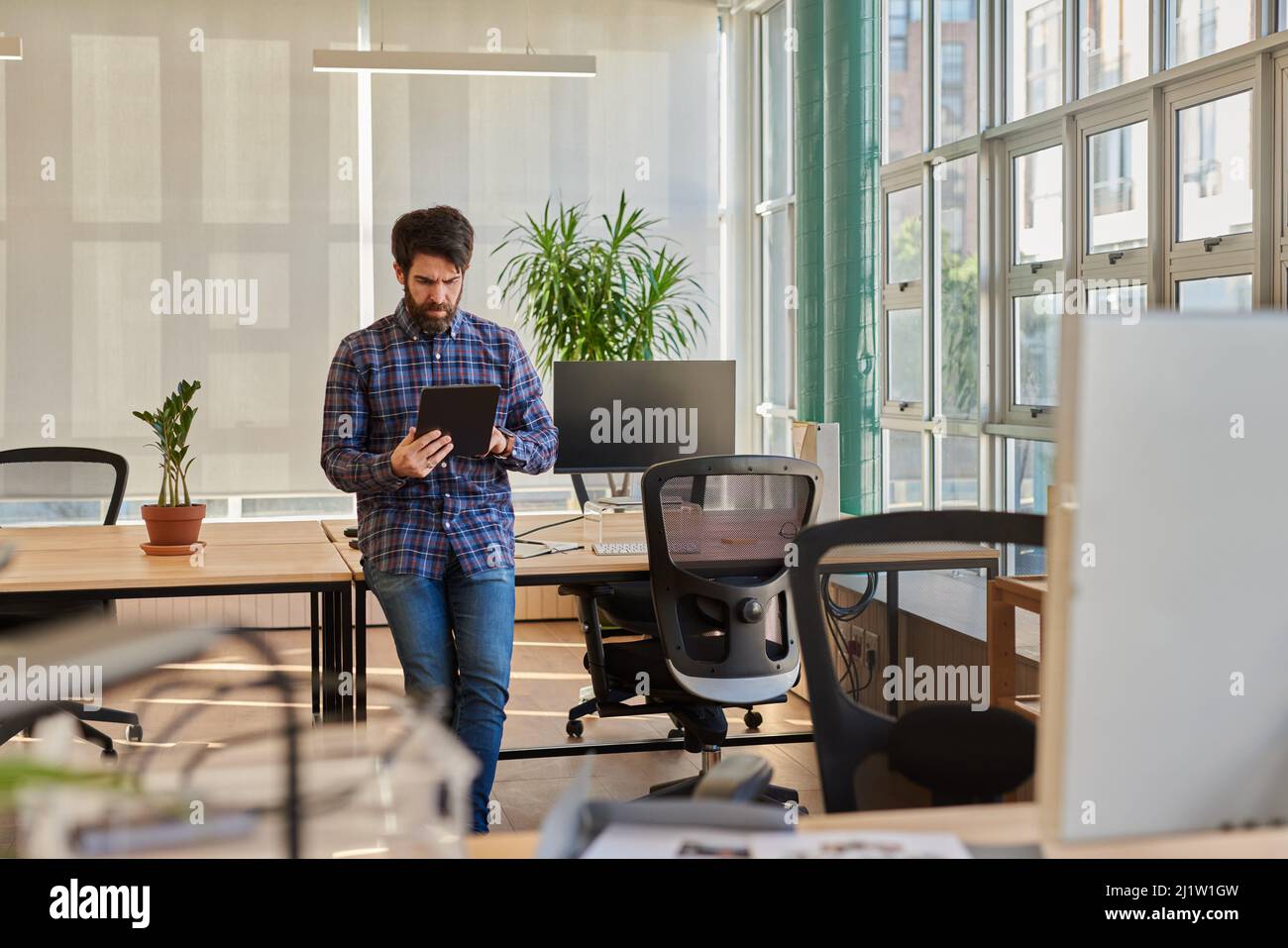Joven hombre de negocios apoyado en su escritorio trabajando en una tableta digital Foto de stock