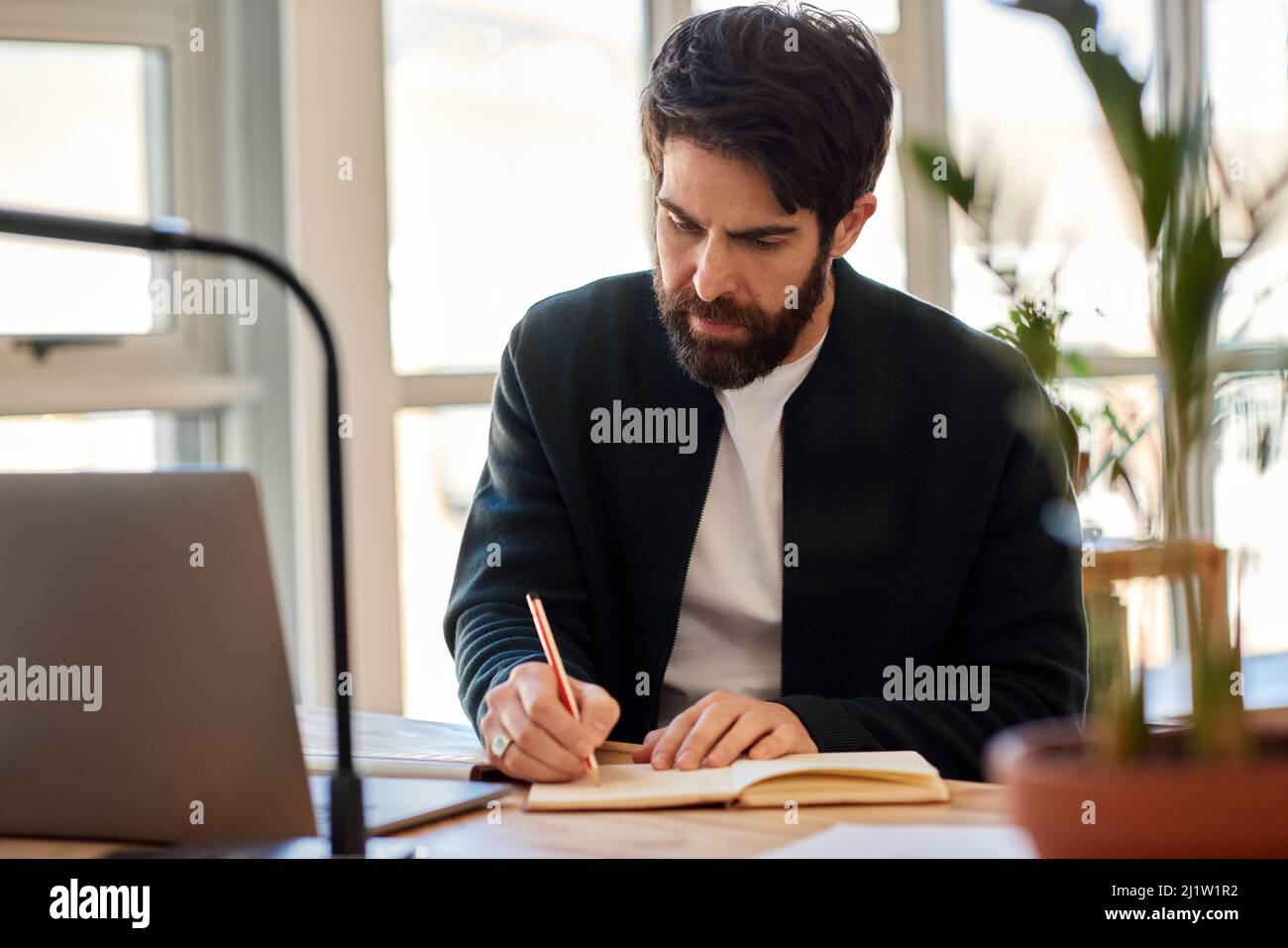 Un joven hombre de negocios escribiendo notas mientras trabaja en su escritorio de oficina Foto de stock