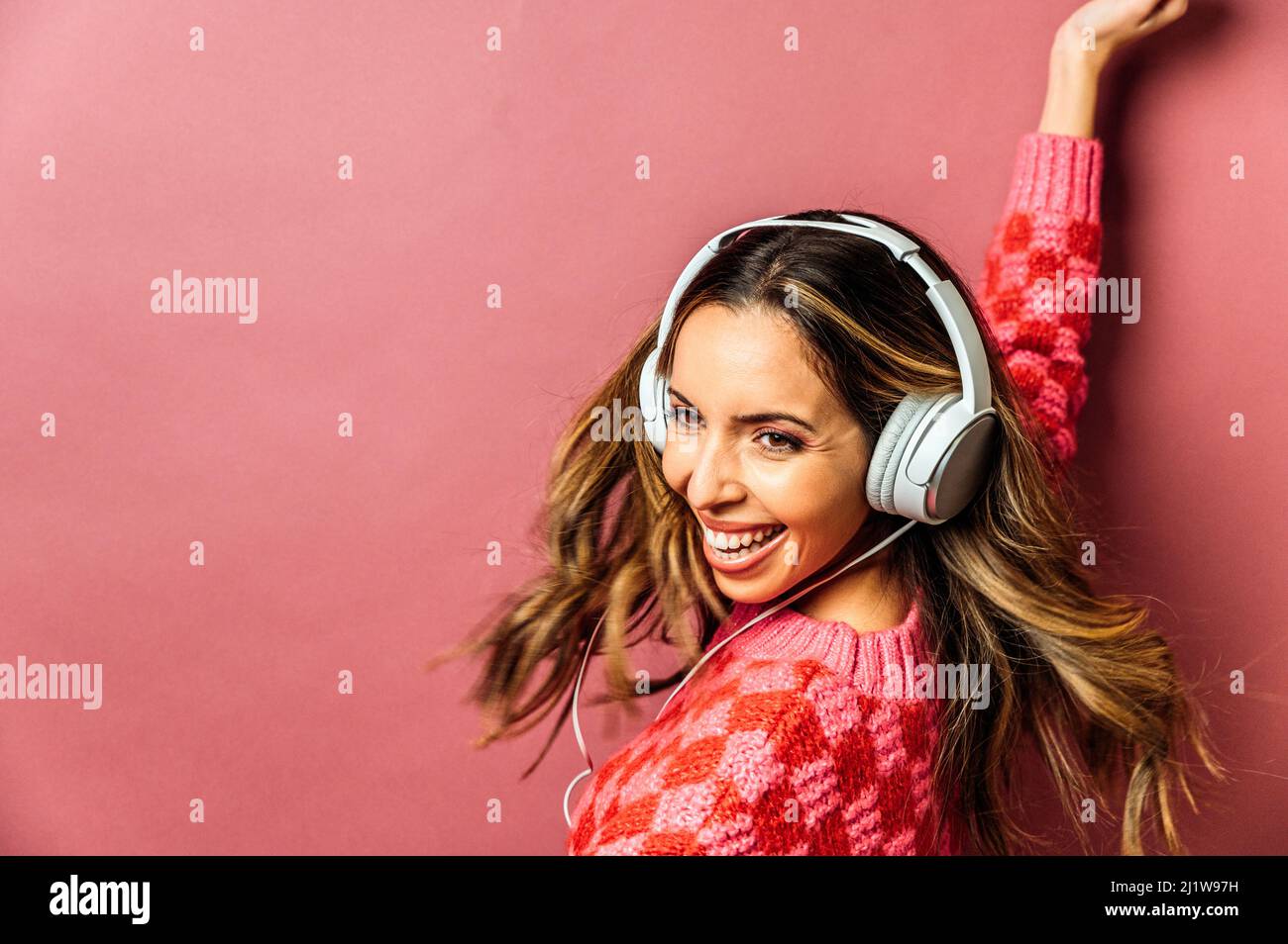 Mujer encantada con el pelo volando escuchando música en los auriculares  mientras se encuentra sobre fondo rosa con la mano elevada en el estudio  Fotografía de stock - Alamy