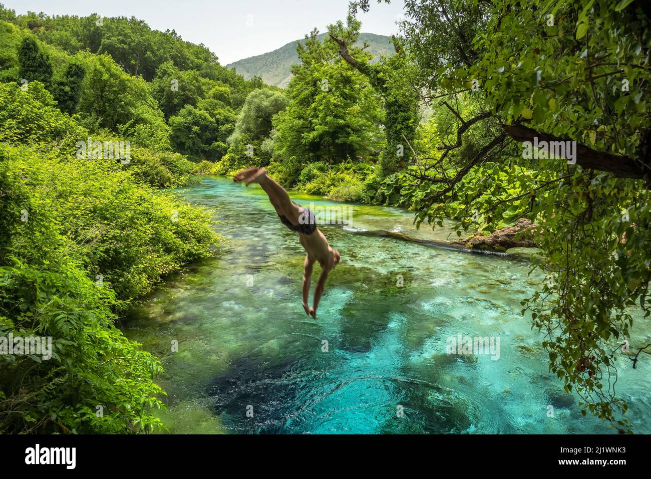 Un hombre no identificado salta al hermoso Blue Eye de la primavera de color turquesa o Syri i Kalter cerca de la ciudad de Muzine en Albania. Foto de stock